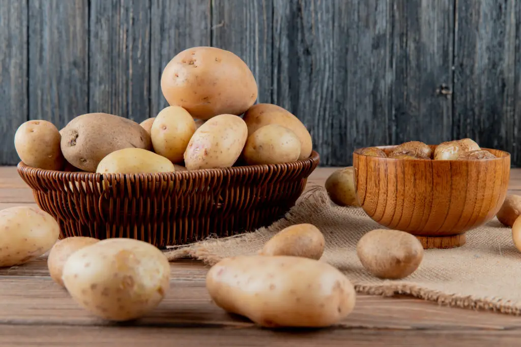 side view of basket and bowl full of potato on sackcloth on wooden surface and background with copy space