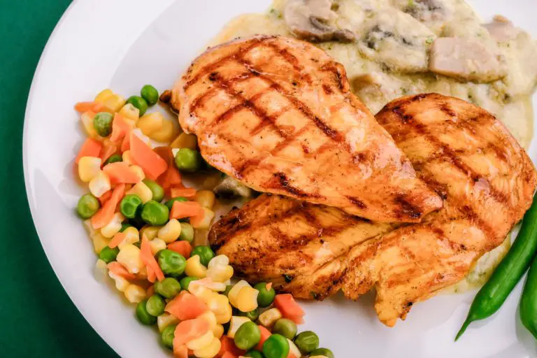grilled chicken breast with green peas and veggies on white plate
